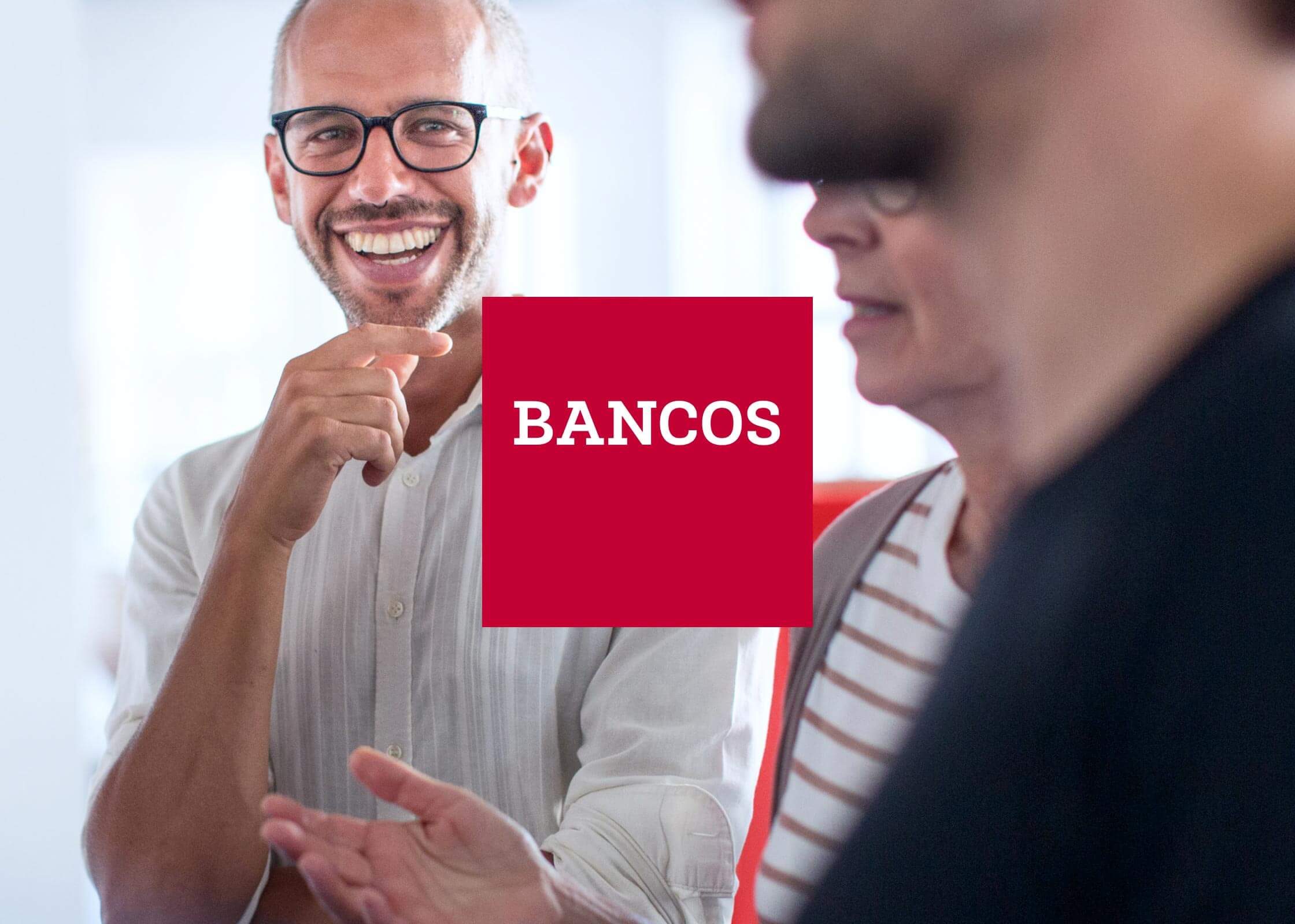 Smiling man in a meeting next to the red square BANCOS logo
